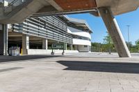 a sidewalk with benches that are under a large bridge to the right of the walkway is a metal frame with concrete columns