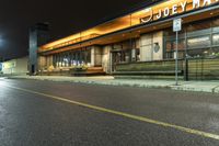 a large parking meter next to a retail area at night with rain on the street