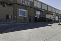 a person on a skateboard in the street in front of an industrial building with a banner