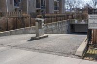 a parking meter in the front of a building near a fence and sidewalk area next to a sidewalk