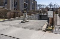 a parking meter in the front of a building near a fence and sidewalk area next to a sidewalk