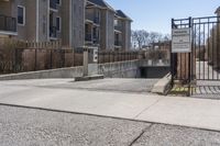 a parking meter in the front of a building near a fence and sidewalk area next to a sidewalk