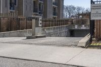 a parking meter in the front of a building near a fence and sidewalk area next to a sidewalk