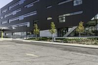 an empty street is lined with green plants and trees in front of the building that's modern