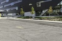 an empty street is lined with green plants and trees in front of the building that's modern