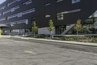 an empty street is lined with green plants and trees in front of the building that's modern