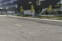 an empty street is lined with green plants and trees in front of the building that's modern