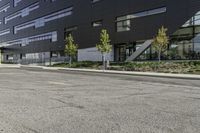 an empty street is lined with green plants and trees in front of the building that's modern