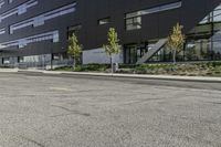 an empty street is lined with green plants and trees in front of the building that's modern