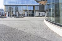 an empty square with glass walls in the background of it and a bus parked in front