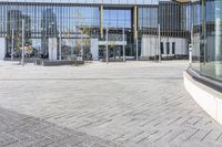 an empty square with glass walls in the background of it and a bus parked in front