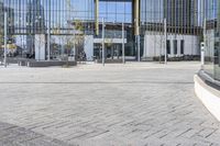 an empty square with glass walls in the background of it and a bus parked in front