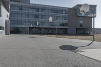 an outdoor basketball court sits in the foreground of the building with the shadow of a basketball net on the ground