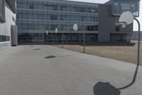 an outdoor basketball court sits in the foreground of the building with the shadow of a basketball net on the ground