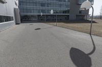 an outdoor basketball court sits in the foreground of the building with the shadow of a basketball net on the ground