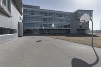 an outdoor basketball court sits in the foreground of the building with the shadow of a basketball net on the ground