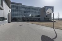 an outdoor basketball court sits in the foreground of the building with the shadow of a basketball net on the ground