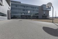 an outdoor basketball court sits in the foreground of the building with the shadow of a basketball net on the ground