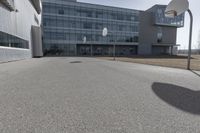 an outdoor basketball court sits in the foreground of the building with the shadow of a basketball net on the ground