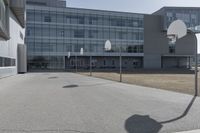 an outdoor basketball court sits in the foreground of the building with the shadow of a basketball net on the ground