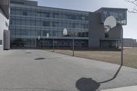 an outdoor basketball court sits in the foreground of the building with the shadow of a basketball net on the ground