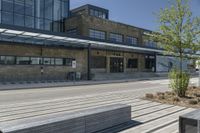 two wooden benches are in front of a large building with windows on the side and skylights above them