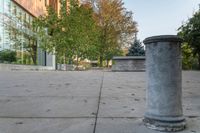 a white garbage can sitting on top of a cement floor next to a building near trees