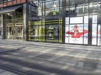 a couple of ads advertises in glass doors on a building with a street and a person standing on the sidewalk