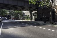 a street with several parked cars and buildings on it in the distance is an empty sidewalk with a fence at one end