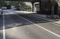 a street with several parked cars and buildings on it in the distance is an empty sidewalk with a fence at one end