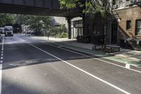 a street with several parked cars and buildings on it in the distance is an empty sidewalk with a fence at one end