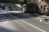 a street with several parked cars and buildings on it in the distance is an empty sidewalk with a fence at one end