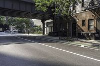 a street with several parked cars and buildings on it in the distance is an empty sidewalk with a fence at one end