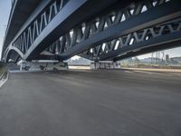 a bike sits underneath an empty, pedestrian bridge during daytime time in a city setting