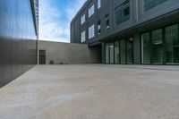 empty concrete sidewalk near large building and windows with doors open and sky above it with clouds