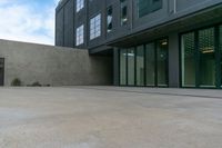 empty concrete sidewalk near large building and windows with doors open and sky above it with clouds