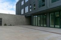 empty concrete sidewalk near large building and windows with doors open and sky above it with clouds