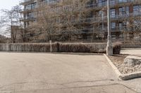 a street has no one that is stopping to walk past a long building and a rock with some grass on it