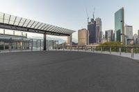 an empty walkway with buildings in the distance behind it and a parking lot with no cars in front