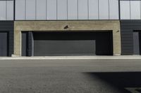 an empty street near a building with a garage on each side of the sidewalk and some windows on top of it