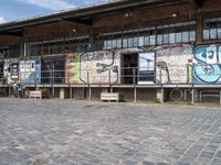 this is an image of a building with graffiti on the walls and benches on the street