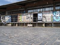 this is an image of a building with graffiti on the walls and benches on the street