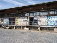 this is an image of a building with graffiti on the walls and benches on the street