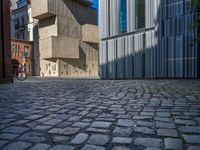 cobblestone driveway surrounded by modern buildings on sunny day with sun reflecting onto the windows