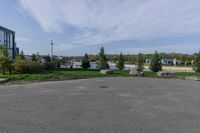 an empty parking lot with trees and lawns along it near buildings and trees in the background