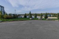 an empty parking lot with trees and lawns along it near buildings and trees in the background