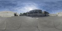 a skateboard park in a city with buildings and blue skies in the background with some clouds