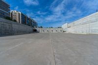 the empty parking lot in front of a wall with apartment buildings on it and a skateboarder on a ramp