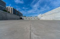 the empty parking lot in front of a wall with apartment buildings on it and a skateboarder on a ramp