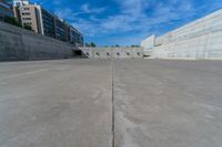 the empty parking lot in front of a wall with apartment buildings on it and a skateboarder on a ramp